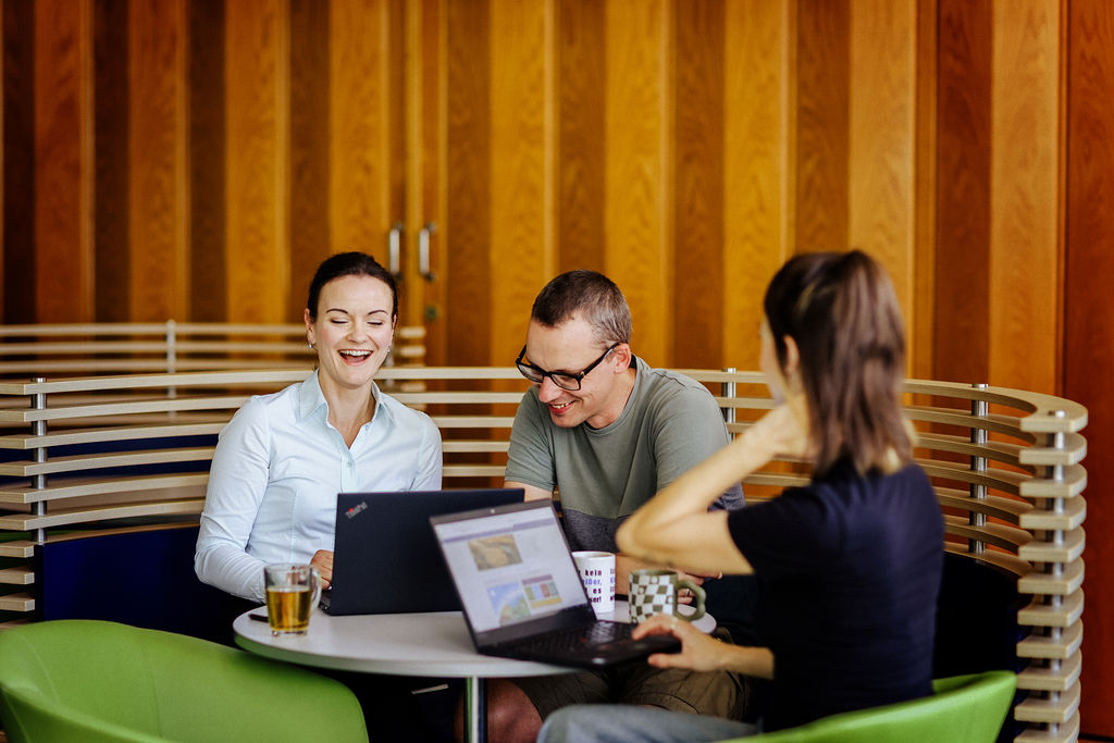 Besprechungssituation Personen mit Laptops lachend am Tisch. Foto: Anne Schwerin