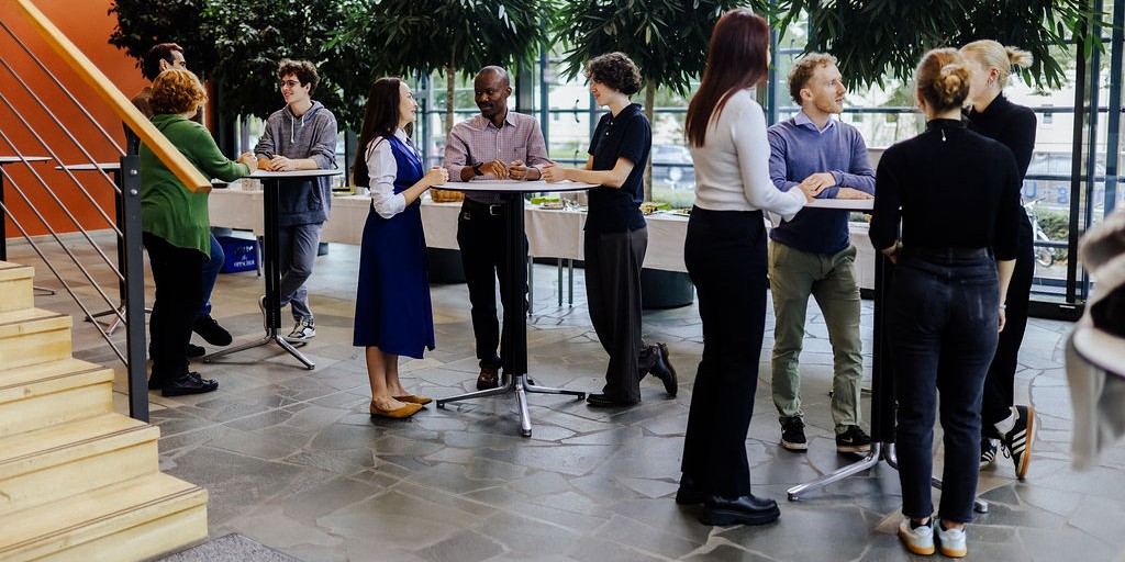 Mehrere Menschen stehen in kleinen Gruppen an Stehtischen in einem Innenraum des Kubus am UFZ und unterhalten sich.