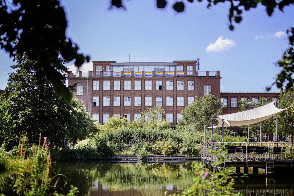 Ein Verwaltungsgeb&auml;ude mit Pride-Fahne, davor der gr&uuml;ne UFZ Campus mit einem Teich. Foto: Anne Schwerin