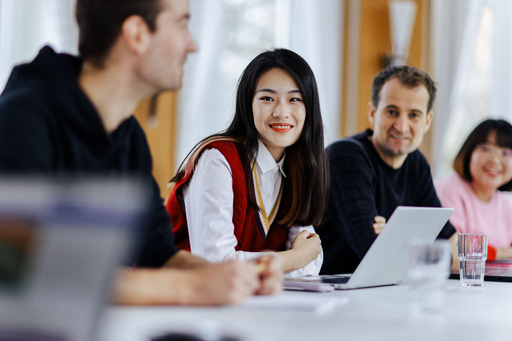 A small group of international people is sitting around a table in a meeting and chatting. Photo: Anne Schwerin